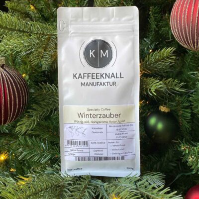 Winterzauber Kaffee von Kaffeeknall – Frontansicht der weißen Packung im weihnachtlich dekorierten Tannenbaum