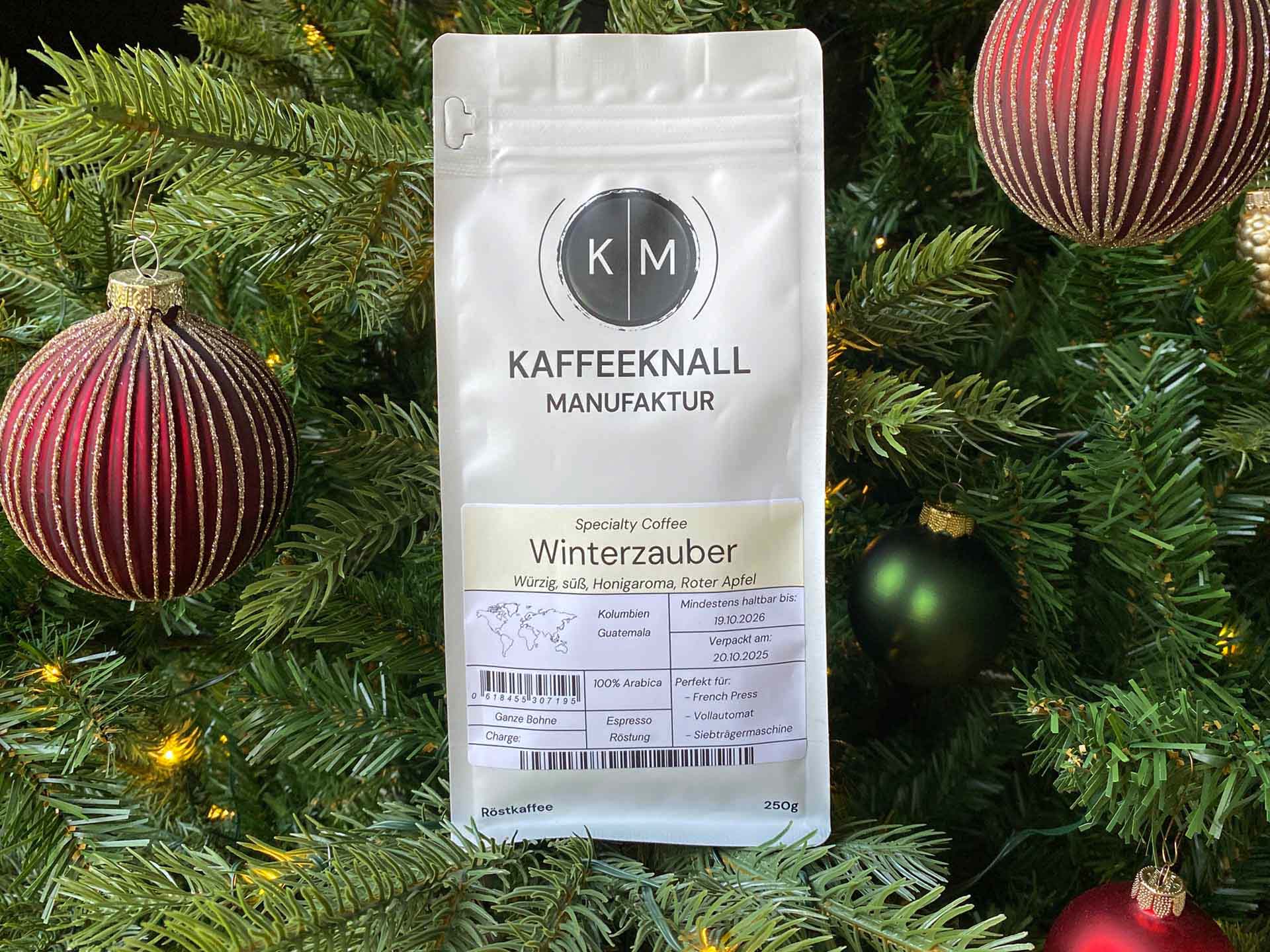 Winterzauber Kaffee von Kaffeeknall – Frontansicht der weißen Packung im weihnachtlich dekorierten Tannenbaum
